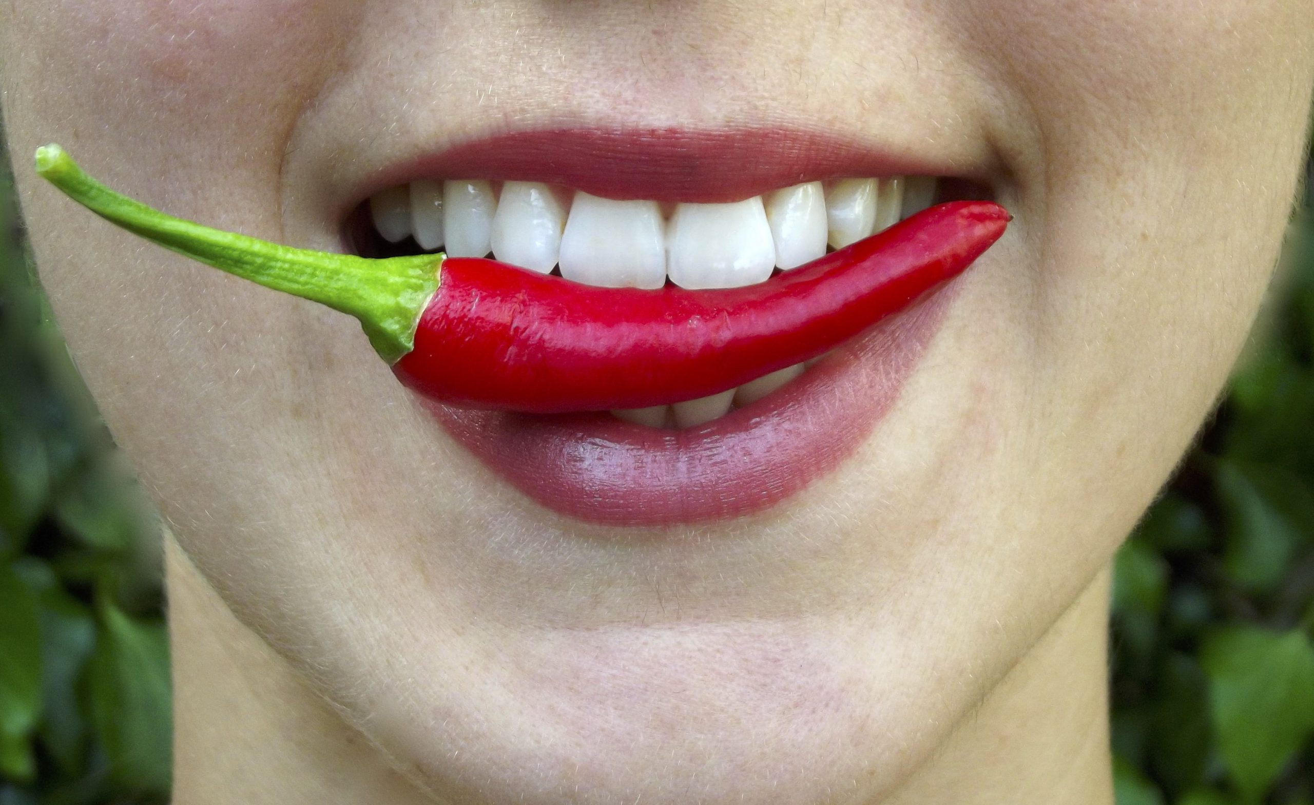 Frau mit einer Chili zwischen den Zähnen