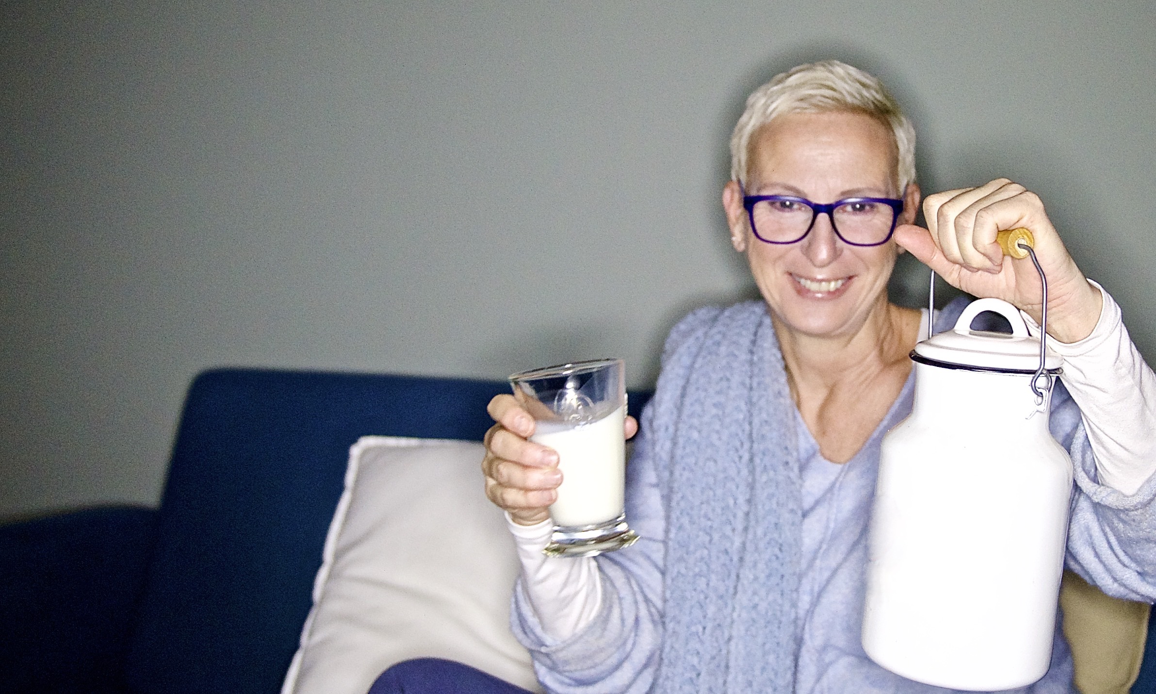 Frau mit Milchkanne und Glas Milch in der Hand